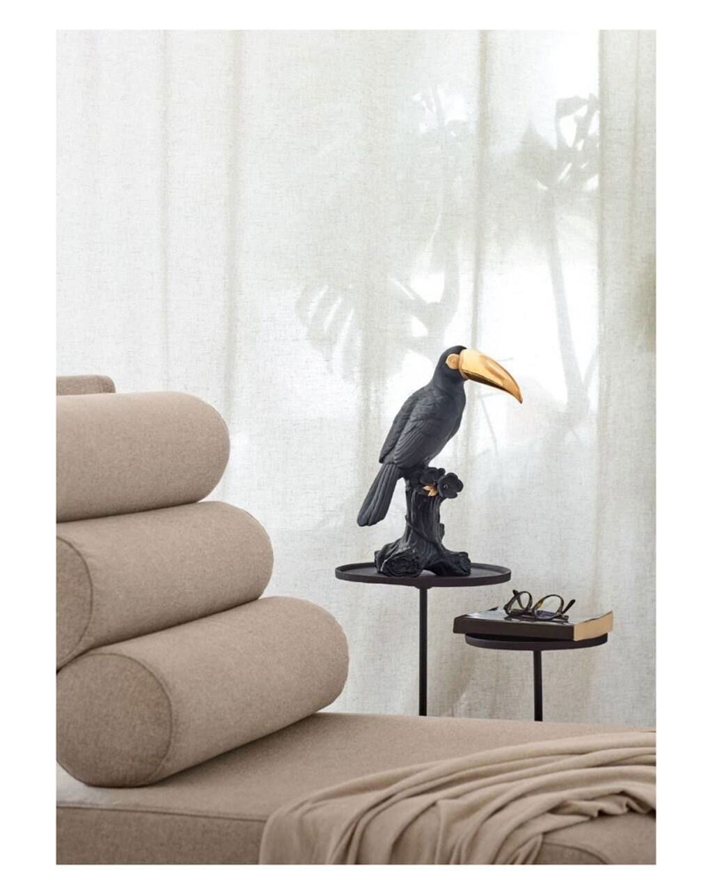Чёрная декоративная фигура птицы с золотым клювом на маленьком столике рядом с бежевым модульным диваном — акцентная деталь интерьера.
