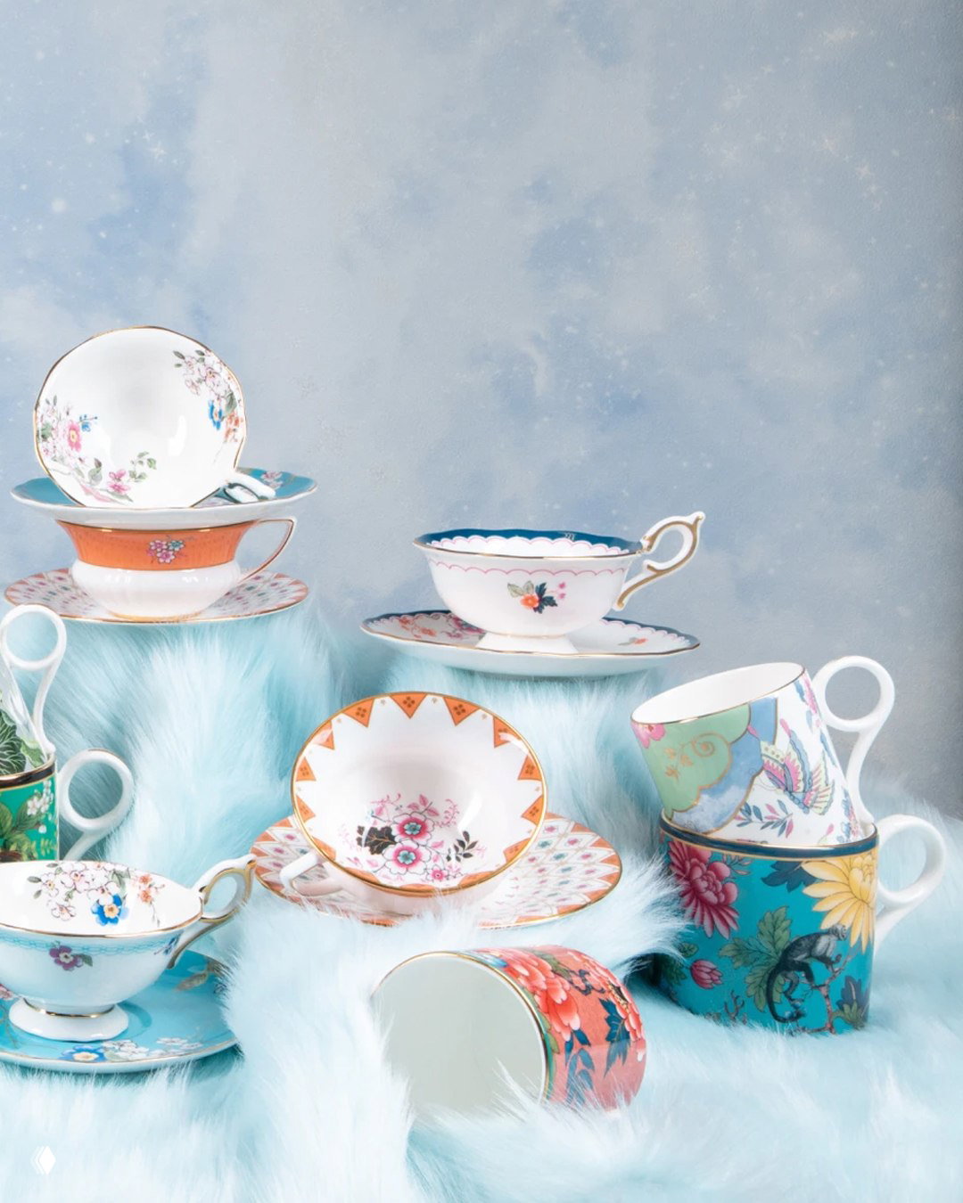 Набор разных чашек и блюдец Wedgwood: утонченный фарфор с флористическими мотивами, сложенный на пушистом голубом текстильном фоне в студийной съемке.