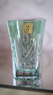Зелёный стеклянный стакан бренда Tajima Glass с тонкой объёмной огранкой, выполненной в узоре хризантемы, на отражающей поверхности.