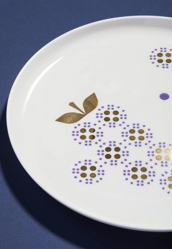 Крупный план декоративного узора: фиолетовые точки и золотые листочки на белой фарфоровой тарелке из сервиза Shirokov.