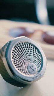 Крупный план аромадиспенсера или автомобильного диффузора с логотипом V, демонстрация компактного аксессуара для персонального аромата в движении.