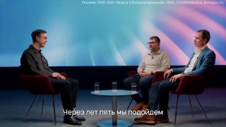 Скриншот интервью: ведущий слева и двое гостей справа сидят в креслах в студии на фоне размытых цветных панелей.