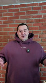 Мужчина в фиолетовом худи на фоне кирпичной стены, с петличным микрофоном на груди — кадр из видео-победителя конкурса, демонстрирующий живое рабочее пространство аптеки.