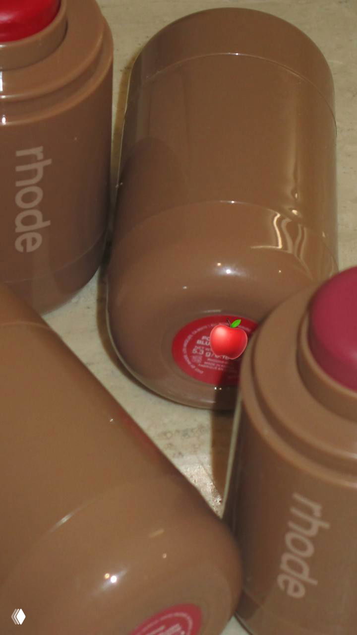 Несколько стиковых упаковок rhode в фирменном бежевом корпусе, видна надпись бренда и открытый стик с насыщенным красным оттенком.