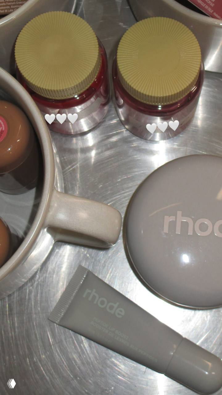 Флэтлей с продуктами rhode: компакт, тюбик и баночки на металлическом подносе, создающие общий взгляд на ассортимент и упаковку бренда.