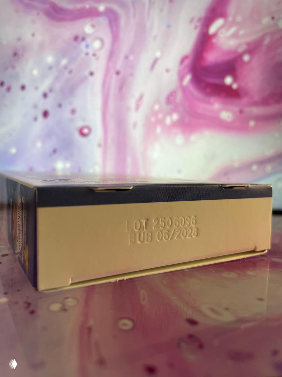 Нижняя часть коробки Carlson с тиснением LOT 2506096 и BUB 06/2028 на фоне розовых разводов — фотография серийного номера и срока годности.