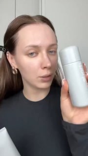 Кадр: женщина показывает флакон Glazing Milk крупным планом на нейтральном фоне, упаковка и этикетка различимы.