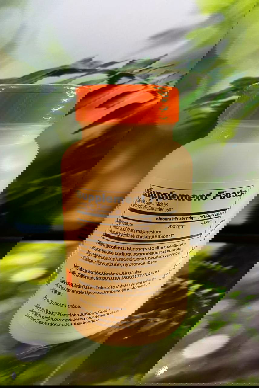 Задняя сторона упаковки Doctor's Best High Absorption Magnesium: таблица Supplement Facts с указанием дозы и состава добавки на фоне зелёных листьев.