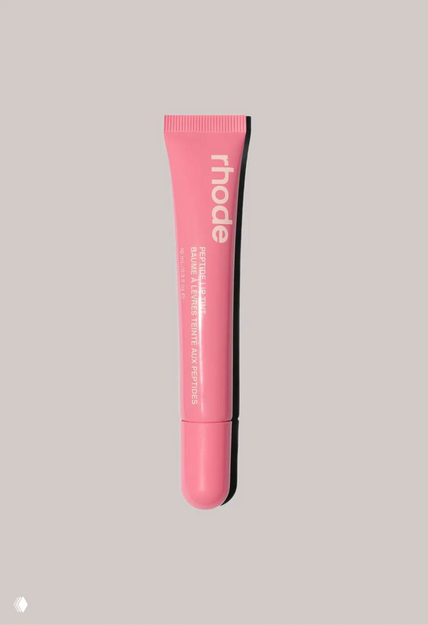 Вертикально ориентированный тюбик rhode пастельно-розового цвета на бежевом фоне; подчёркнут минималистичный дизайн и цвет корпуса упаковки