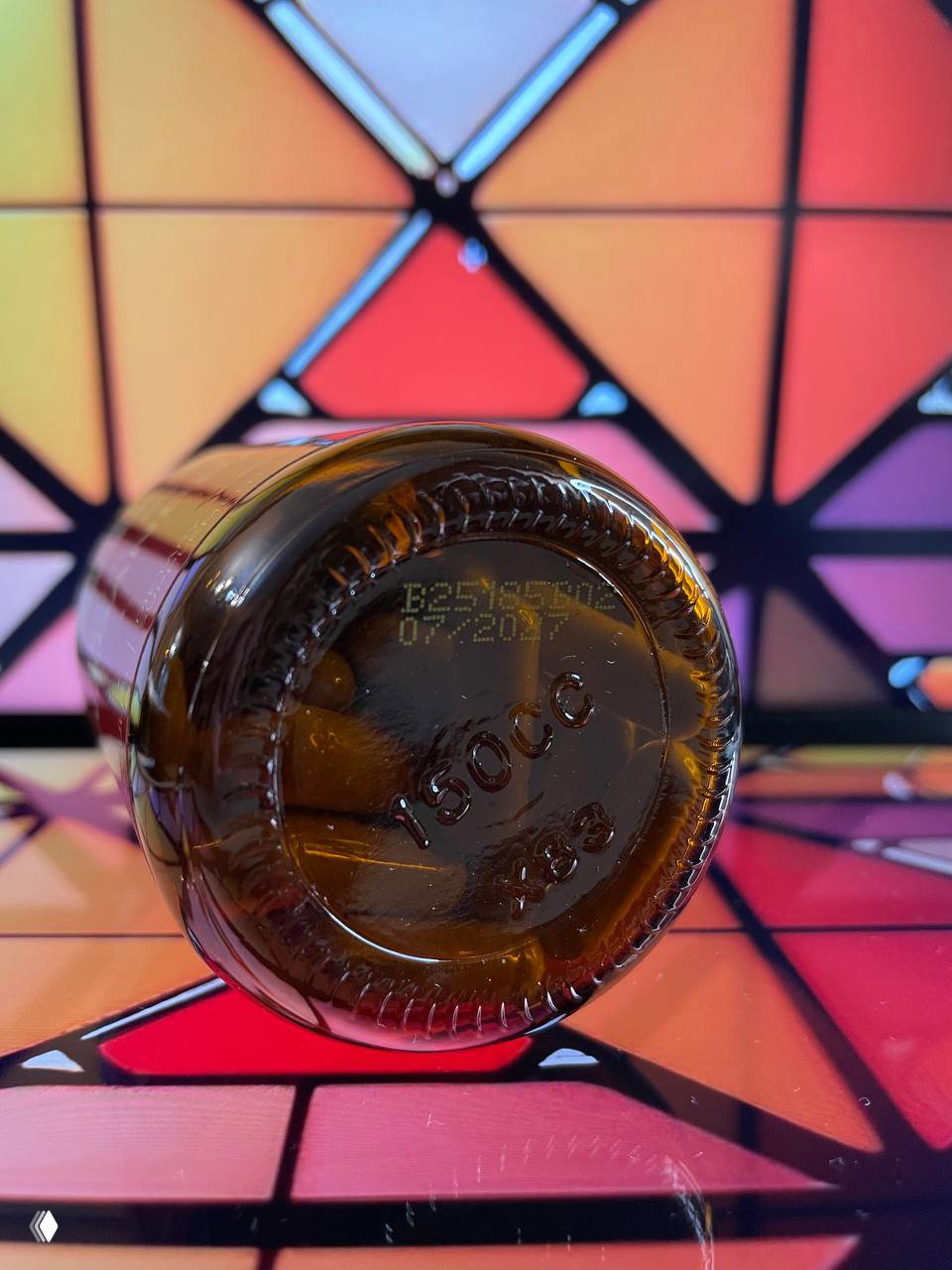 Дно стеклянной банки с нанесённым кодом и датой срока годности 07/27, видны гравировка и отражение на поверхности на цветном фоне.