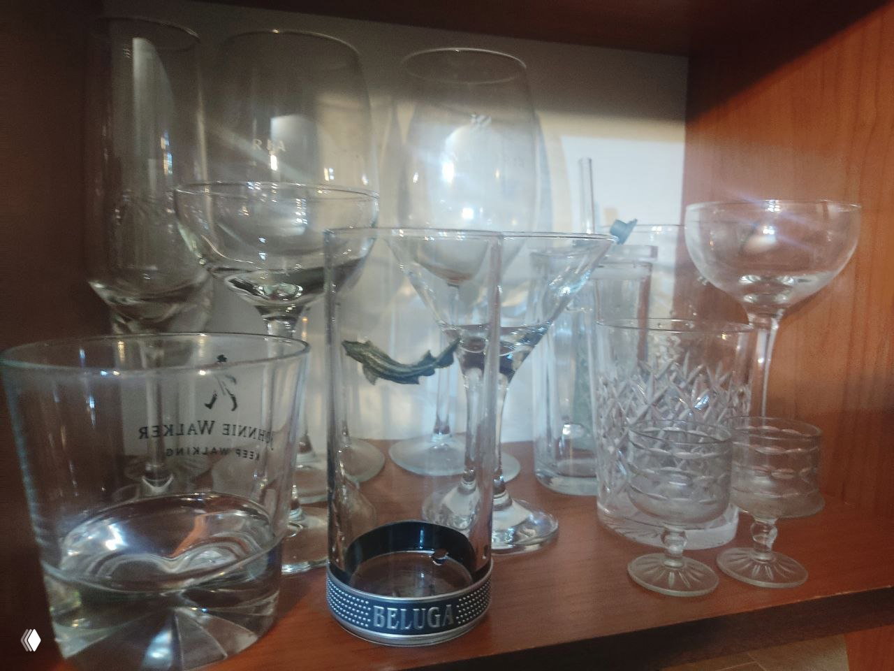 Полка домашнего бара с разнообразными бокалами: роксы, коктейльные рюмки, стопки и купе; на переднем плане шот со шильдиком Beluga.