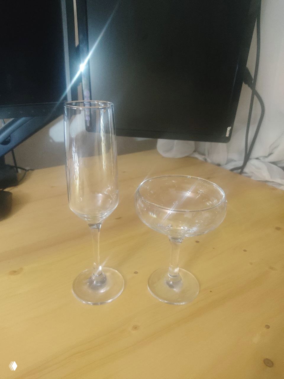 Флейта и купе на деревянном столе на фоне монитора — пример бокалов для шампанских и коктейлей в домашнем баре.