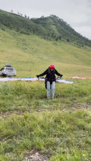 Ученик на травяном склоне выполняет разбег и наземную отработку управления куполом в условиях переменчивой погоды.