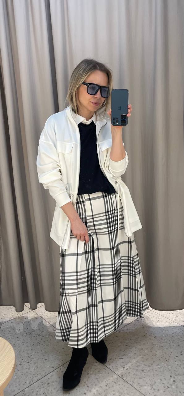 Белая парка, чёрный свитер и клетчатая юбка в примерочной — ещё один вариант комбинирования предметов из одной капсулы.