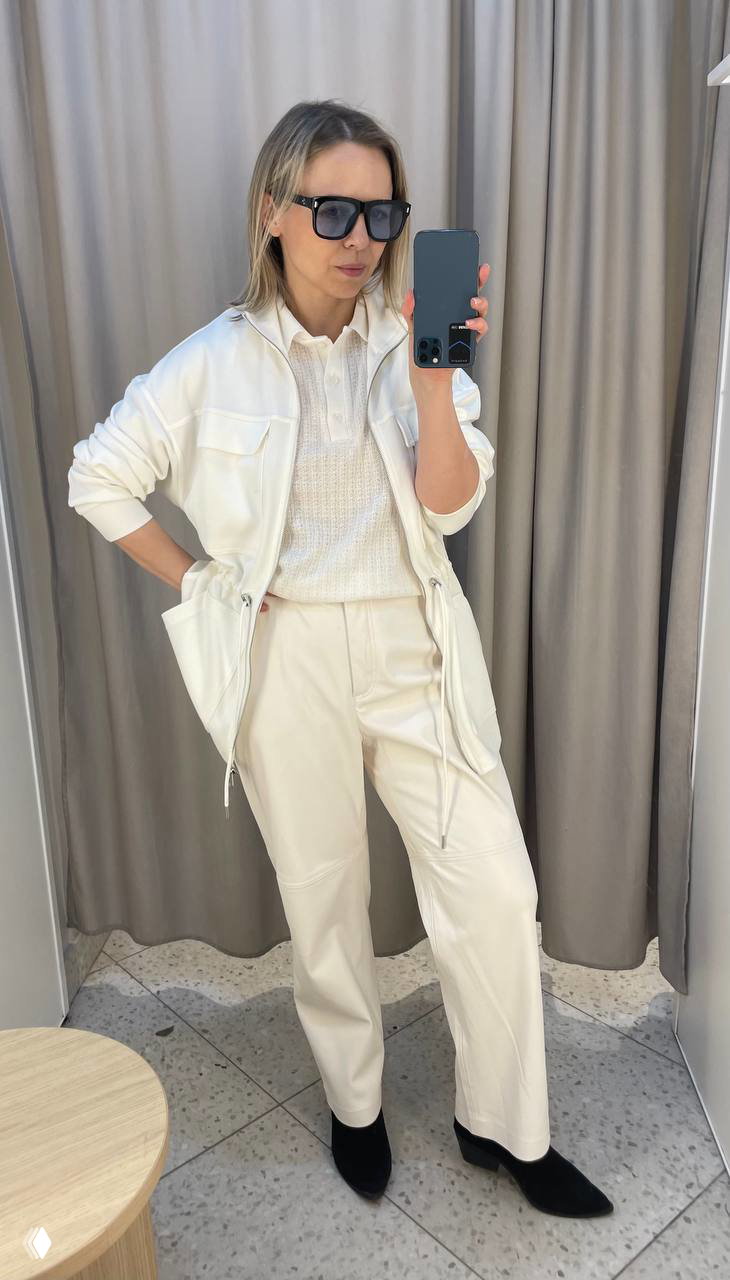 Полный рост в светлом комплекте: белая парка, вязаный поло и светлые брюки — нейтральный рабочий образ на весну и лето.