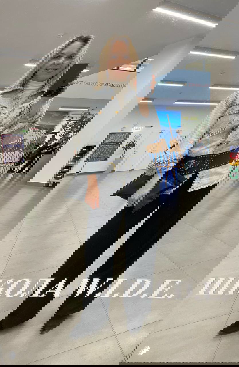 Зеркальное селфи с джинсовой рубашкой, широкими чёрными брюками и поясом; образ в стиле casual с клатчем на фоне холла и мольбертов.