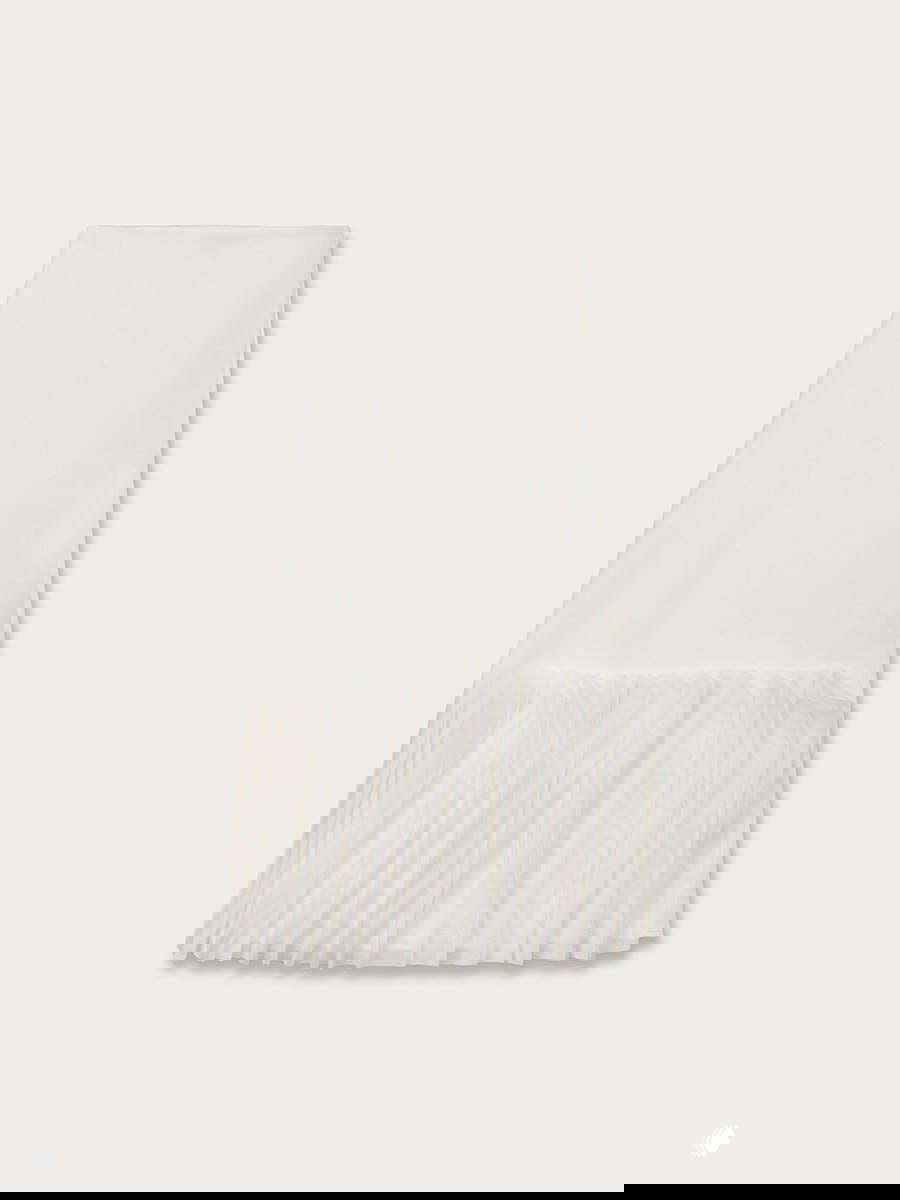 Фото белой юбки с рюшем внизу на нейтральном фоне — демонстрация фактуры и длины для составления летней капсулы.