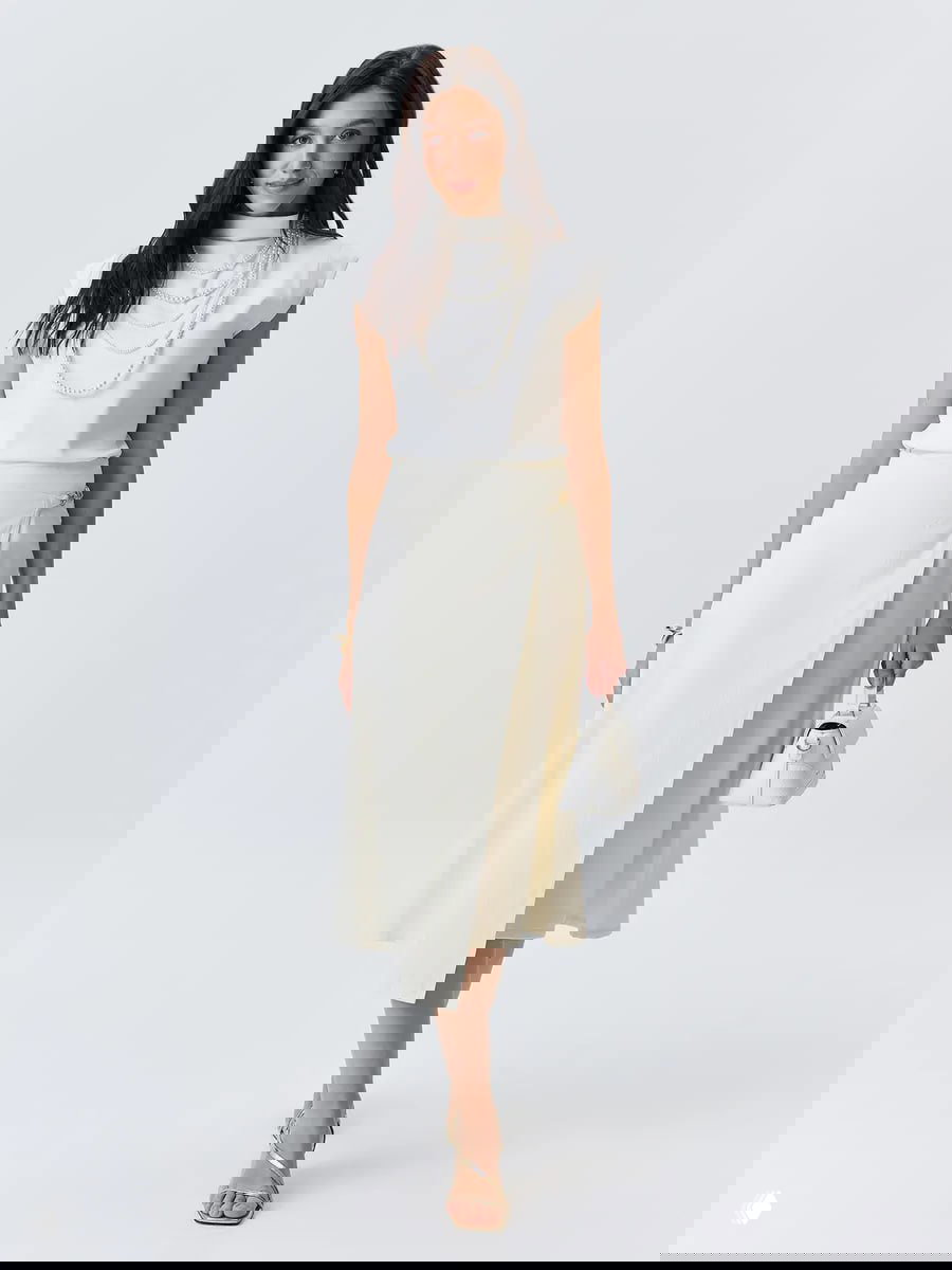 Кремовая юбка на запах в сочетании с белой блузой и мини-сумкой; лёгкий элегантный образ для повседневной носки и прогулок.