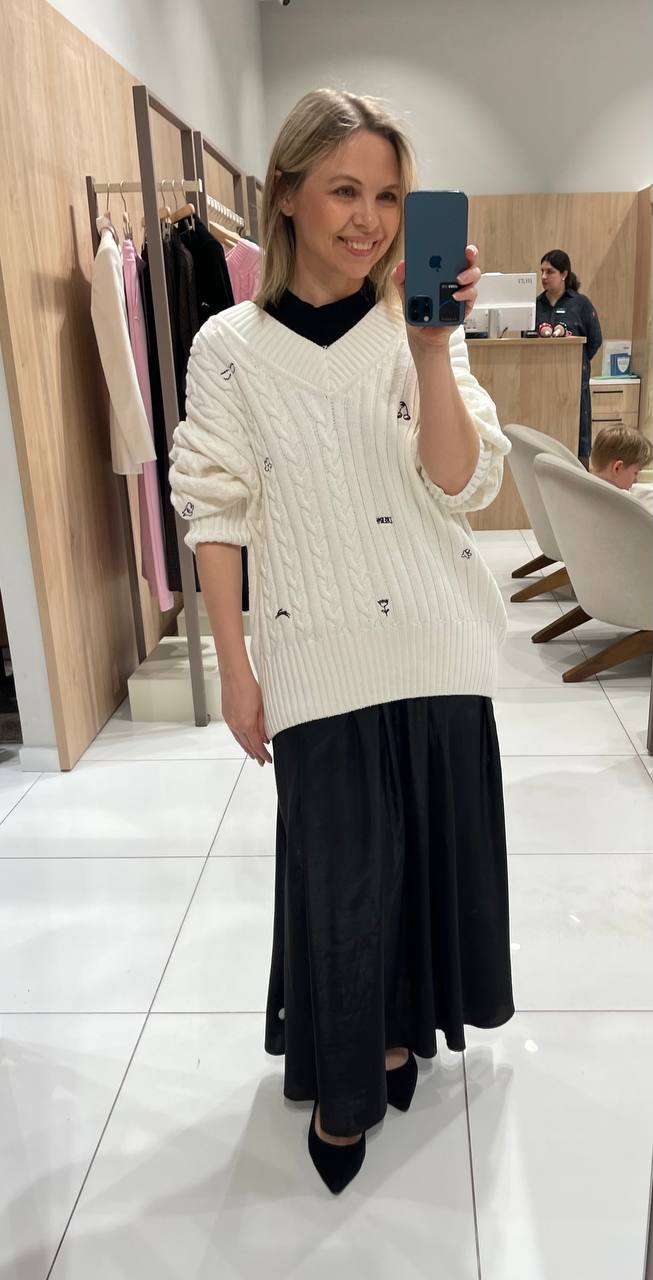 Селфи в зеркале: тёплый вязаный свитер поверх чёрной юбки в просторной примерочной с минималистичным интерьером магазина.