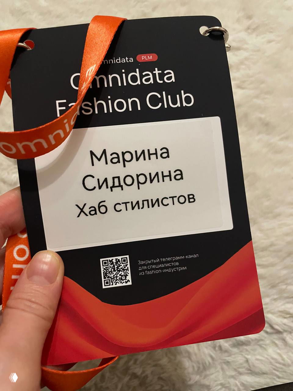 Крупный план бейджа Omnidata Fashion Club с именем «Марина Сидорина Хаб стилистов» на оранжевой ленте и графическим оформлением карточки.