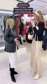 Две женщины в шоуруме обсуждают образ: Марина и Виолетта у вешалок; видны пиджак, белая юбка в горошек, сапоги и примерочная обстановка.