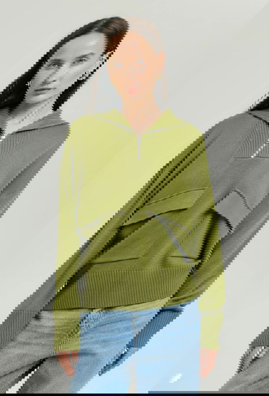 Модель в зелёном трикотажном свитере с передними карманами и молнией, расслабленный офисный образ в сочетании с голубыми джинсами.