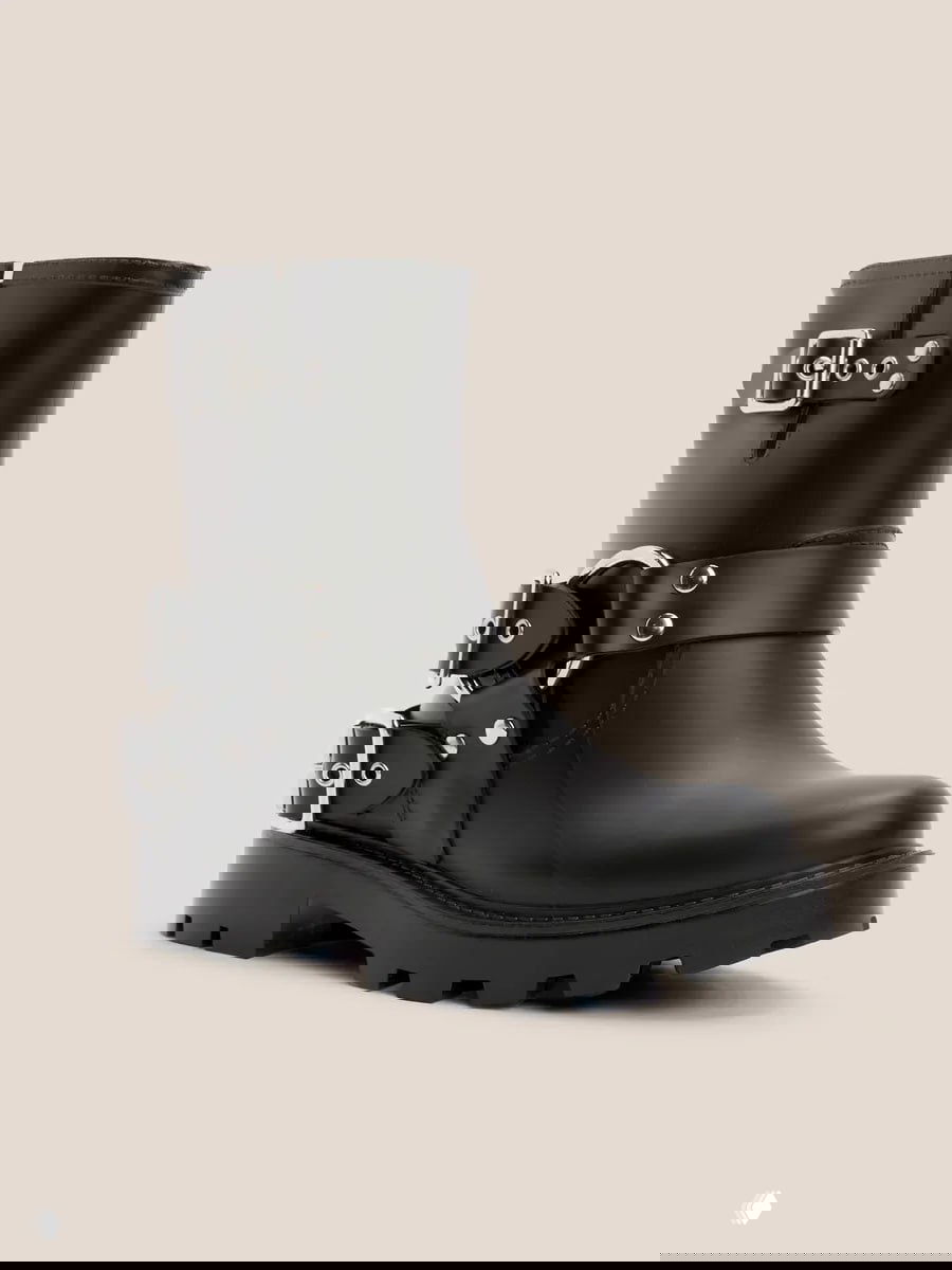 Чёрные резиновые ботинки с декоративными пряжками и массивной подошвой на нейтральном фоне, брутальный стиль средней высоты голенища.