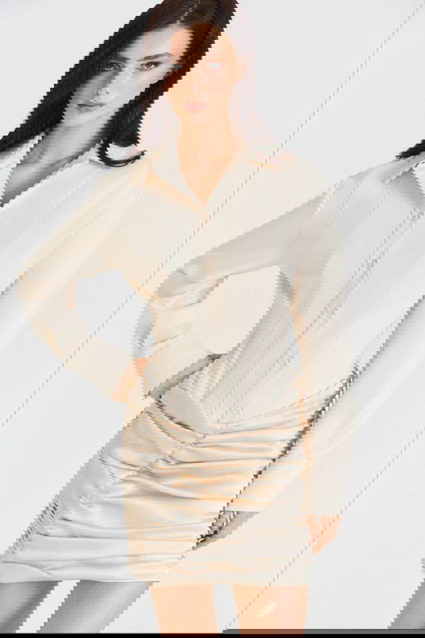 Модель в молочно‑белой приталенной блузе и драпированной мини‑юбке, студийная съёмка, вид по корпусу, подчёркнутые линии талии.