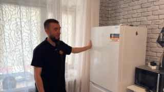 Мастер стоит возле холодильника Indesit в кухне — демонстрация внешнего осмотра и обсуждение возможной поломки компрессора и способов экономии на ремонте.