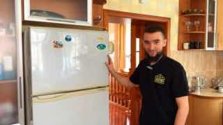 Мастер у холодильника Daewoo в домашней кухне: мужчина в тёмной рубашке стоит рядом со старым двухдверным холодильником с магнитами; видна мебель и кухонный интерьер.