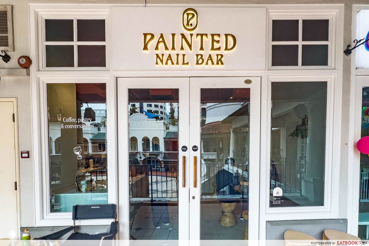 Вход Painted Nail Bar @ The Cathay в Сингапуре: белые рамы, золотая вывеска Painted Nail Bar и стеклянные двери с видом на интерьер и кофейный уголок.