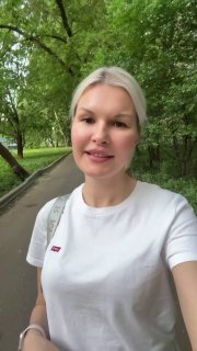 Портрет Ольги Аряевой на аллее в парке: улыбающееся лицо в белой футболке, зелёные деревья и дорожка позади.
