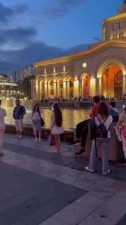Вечерняя набережная города с подсвеченным зданием и людьми, собравшимися у воды — городская вечерняя атмосфера и прогулки.