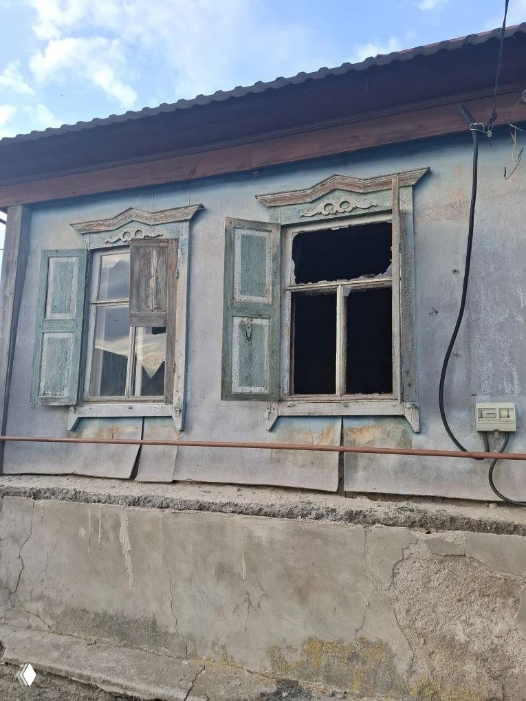 Фасад старого деревянного дома с выбитыми окнами и обгоревшими наличниками: видны разрушения после возгорания, открытые проёмы и следы гари на раме.
