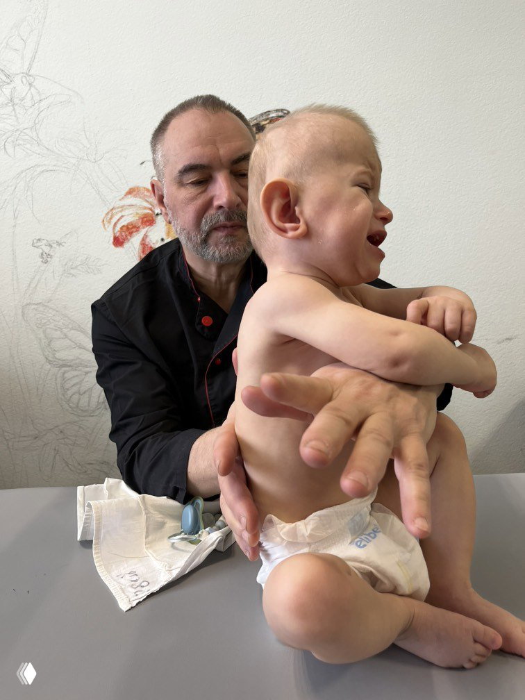 Врач или специалист держит одного из мальчиков на приёме — фотография демонстрирует процесс медицинского осмотра и терапии.