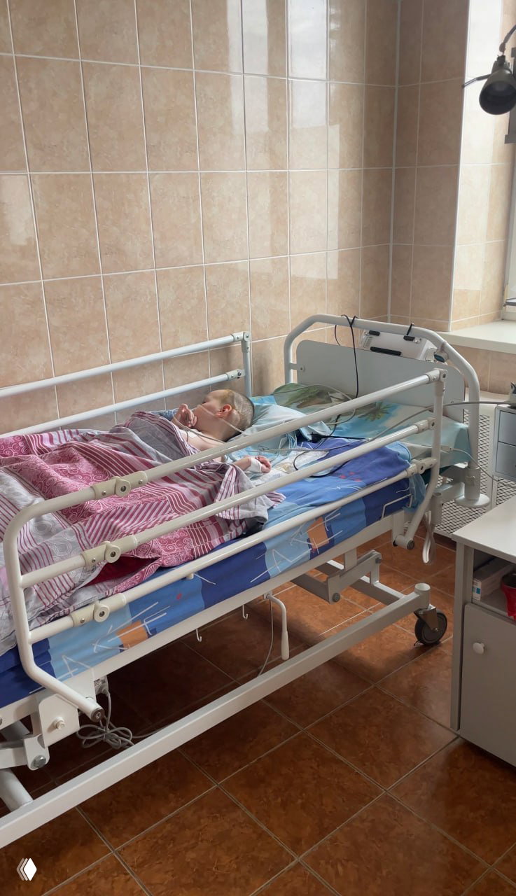 Палата с больничной кроватью, ребёнок лежит подключённый к мониторам и трубкам; типичная медицинская обстановка реабилитации.