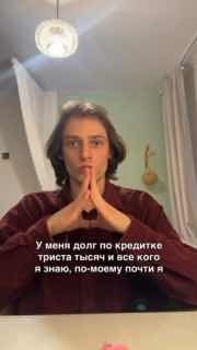 Кадр из вертикального видео: молодой человек стоит в комнате, сложил руки в жесте концентрации, на экране наложен текст о кредите.