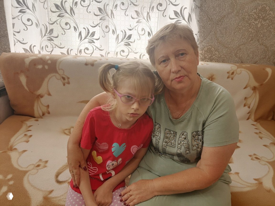 Бабушка и девочка сидят на диване: бабушка обнимает внучку; кадр показывает семейную поддержку и уход за детьми в одной семье.