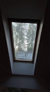 Мансардное окно с видом на заснеженные ветки и морозные узоры на стекле, через которое падает мягкий дневной свет в комнате.