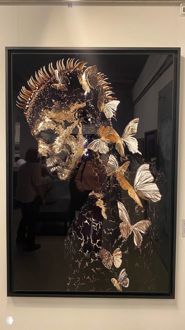 Темная картина с изображением черепа и золотистыми бабочками, экспериментальная современная композиция в рамке на белой стене галереи.