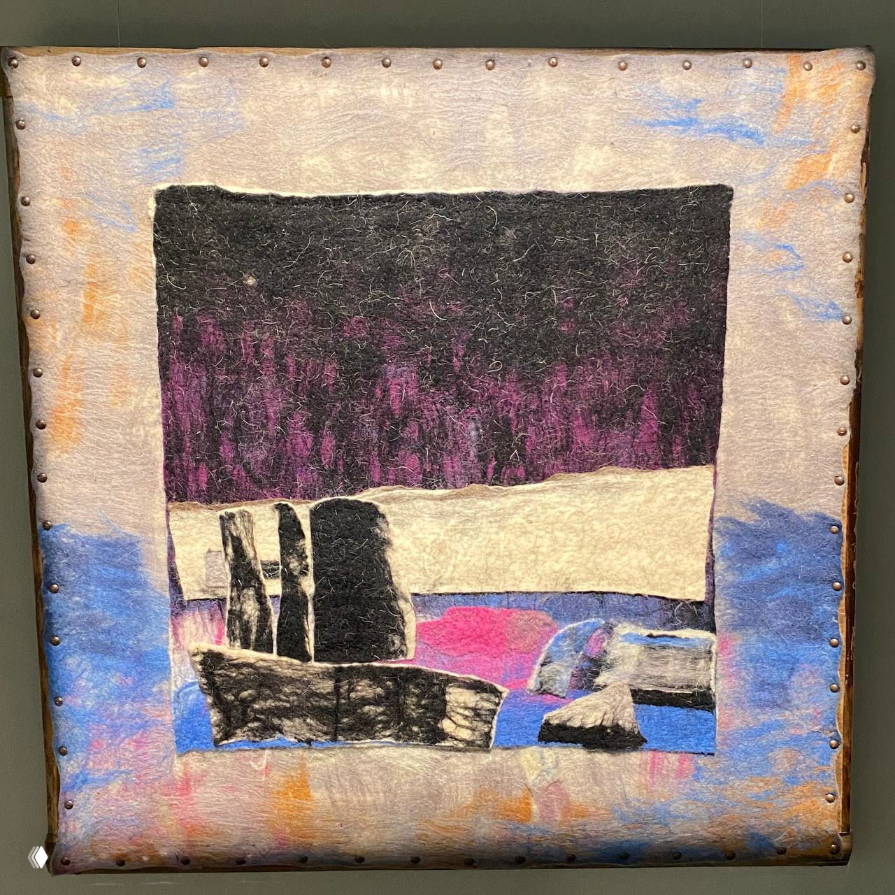 Текстильная или валяная картина в светлой раме с абстрактным ландшафтом и фактурой войлока, оформленная и вывешенная в экспозиции.