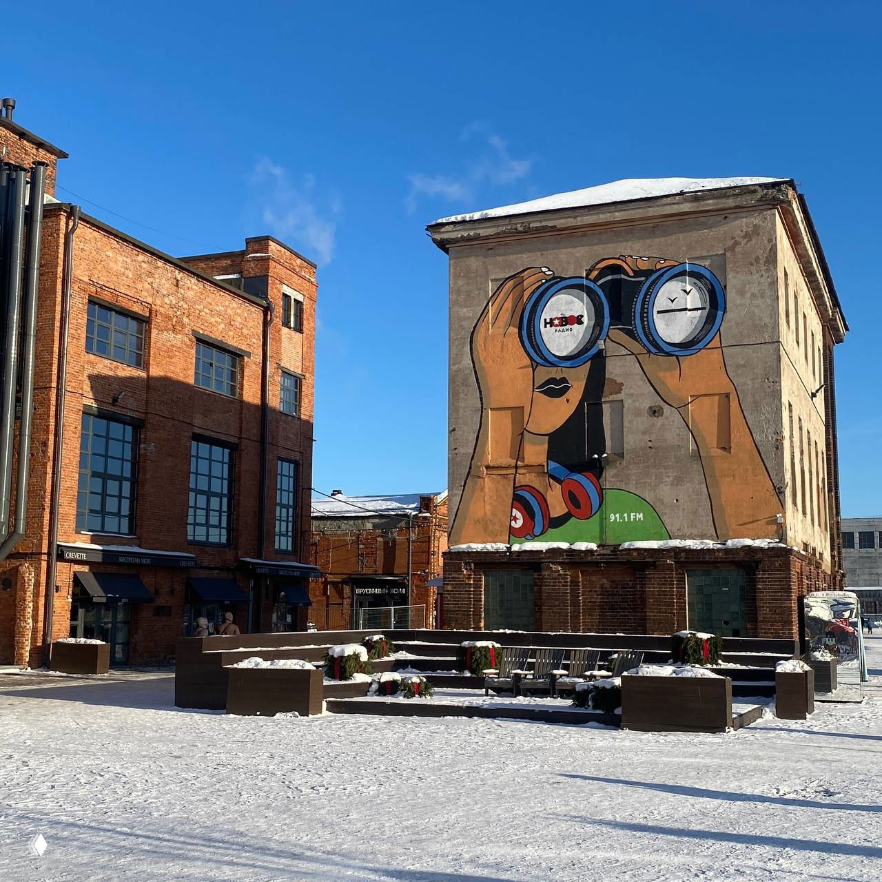 Двор креативного кластера с граффити на стене и красными кирпичными зданиями, солнечная дневная сцена в историческом индустриальном пространстве.