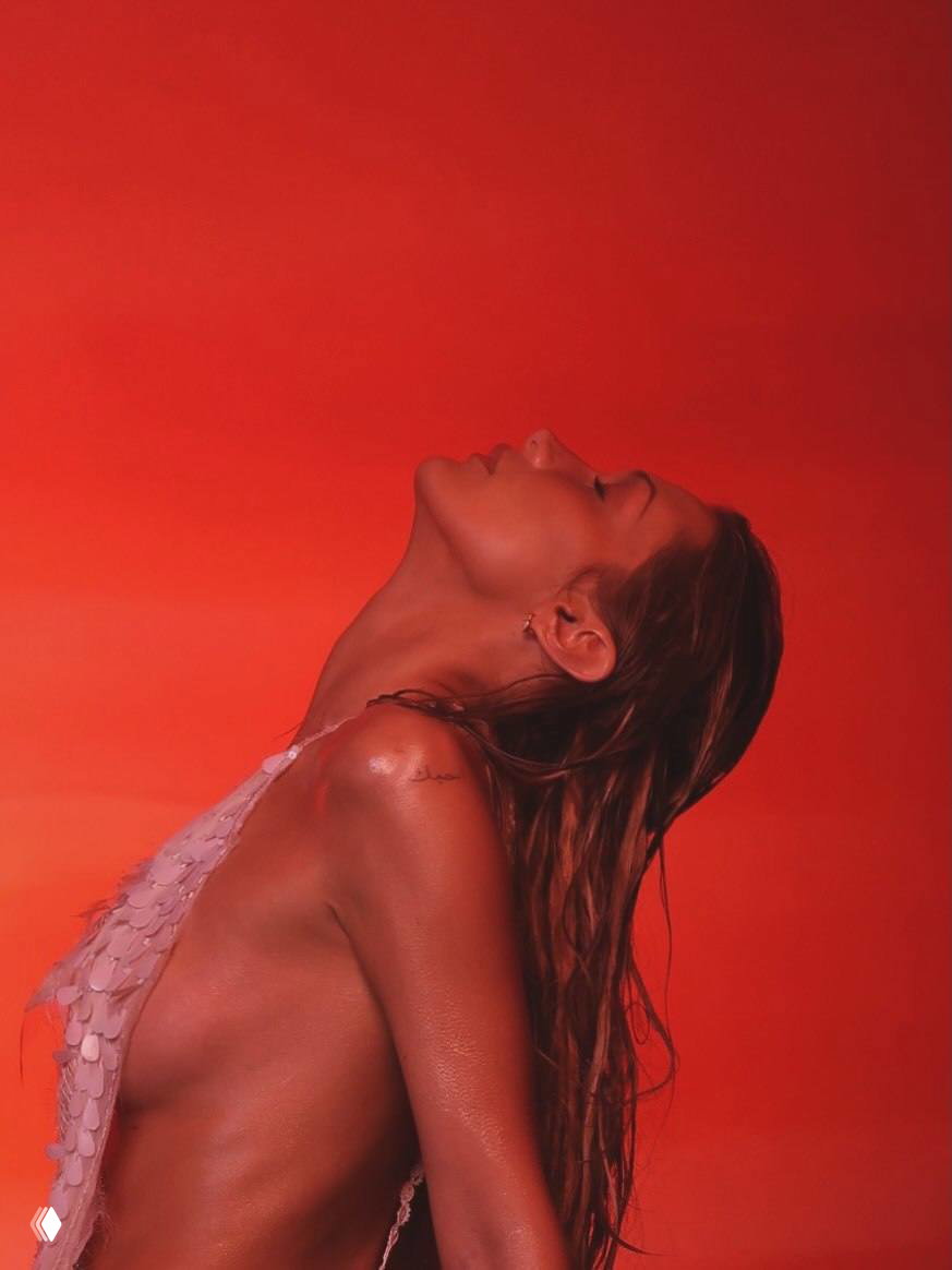 Профиль модели с откинутой головой и влажными волосами на красном фоне; свет подчёркивает контуры шеи и плеч.