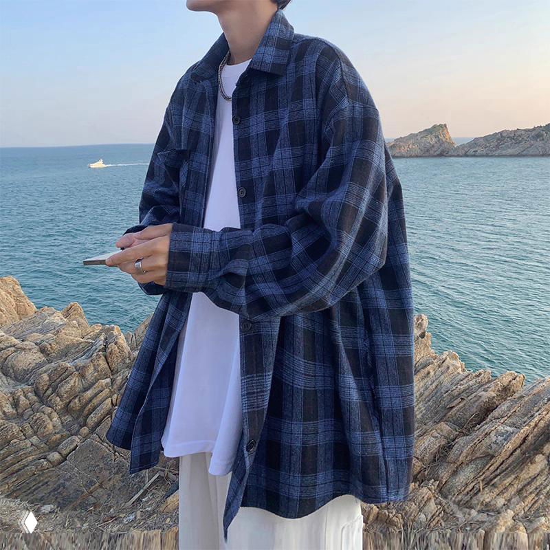 Свободная синяя клетчатая рубашка на человеке у моря, расслабленный образ с белой футболкой и каменным берегом.