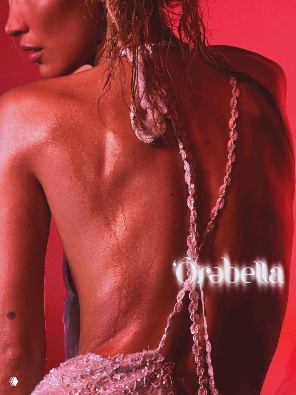 Крупный план спины модели в декорированном платье; на красном фоне виден брендовый логотип в нижней части кадра.