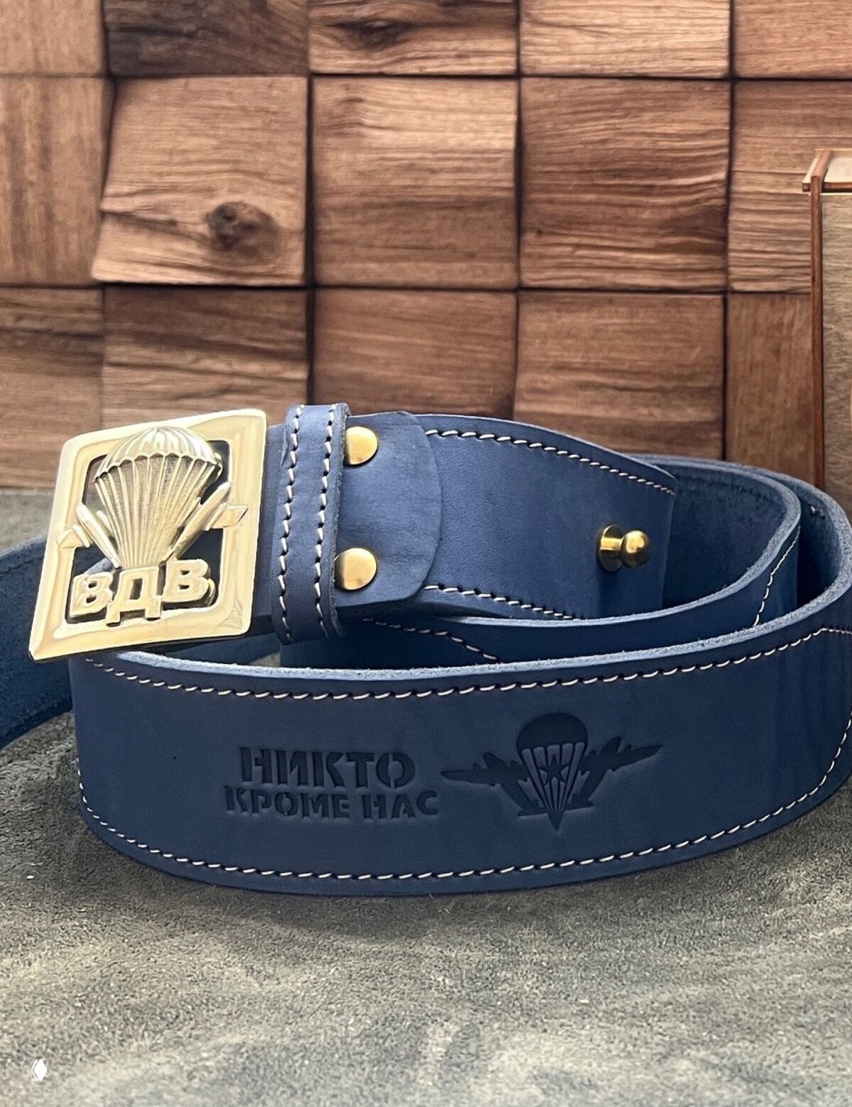 Синий кожаный ремень с пряжкой-парашютом и тисненой надписью «НИКТО КРОМЕ НАС», аккуратная строчка по краю.