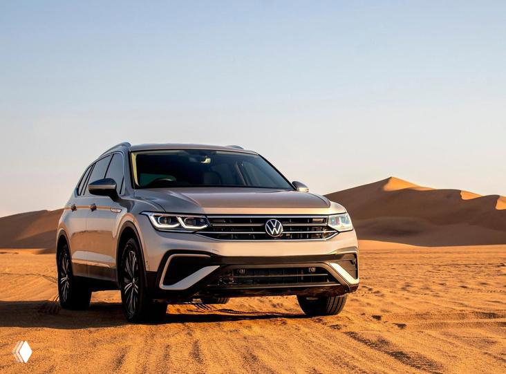 Серебристый Volkswagen Tiguan на фоне песчаных дюн: кроссовер в пейзаже, подчёркнут клиренс и передняя часть автомобиля для внедорожных условий.