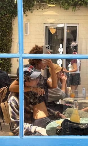 Отражение в окне: пара в кафе, видно, как молодые люди сидят за столиком; кадр сделан из-за стекла на улице в Калифорнии.
