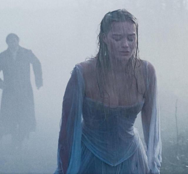 Актриса в промокшем платье с выраженным вырезом стоит под дождём, мокрая ткань и свет выделяют контур декольте в эмоциональной сцене.