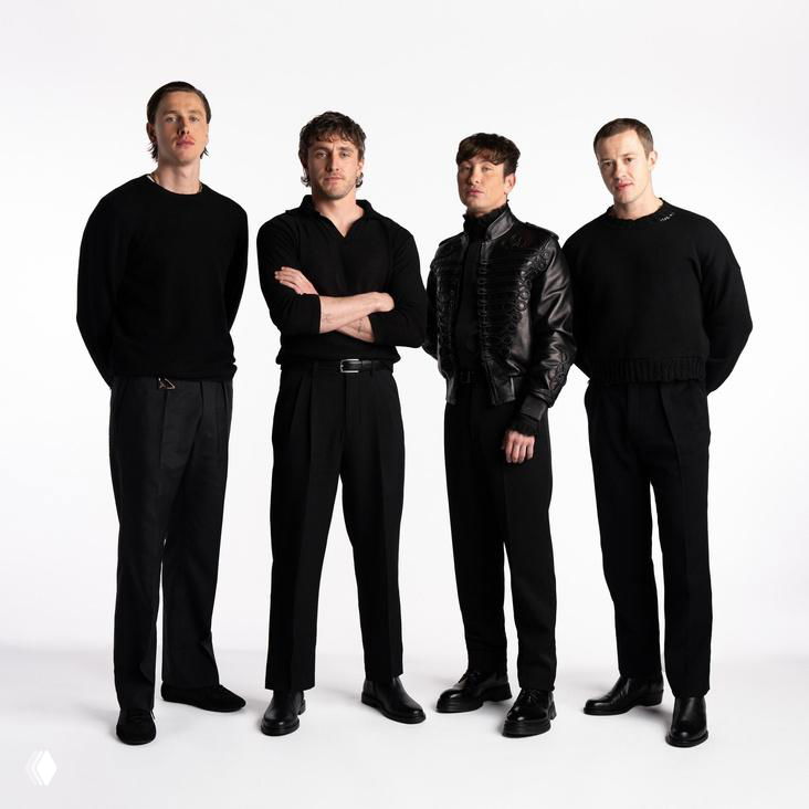 Студийная фотография группы в чёрном: четыре человека в современном минималистичном стиле позируют в полный рост, нейтральный фон.